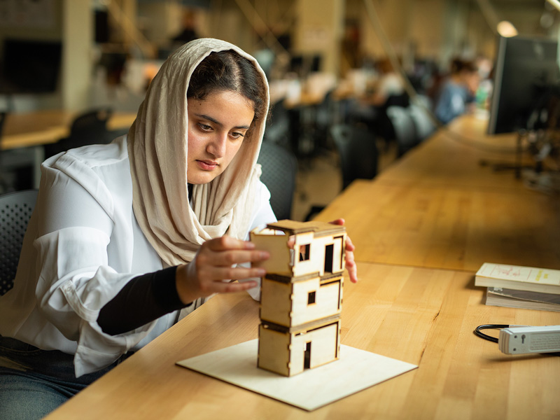A young woman wearing a hijab constructing a small structure from laser cut pieces of wood.