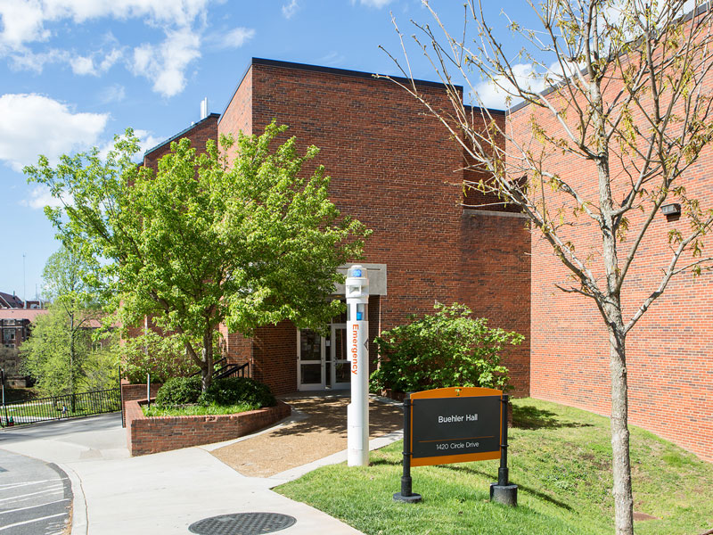 Large red brick building with green trees and lawn surrounding it.