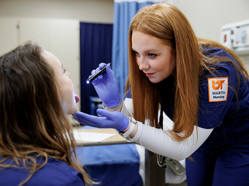 A red-headed nurse uses a pen light to examine a patients mouth.