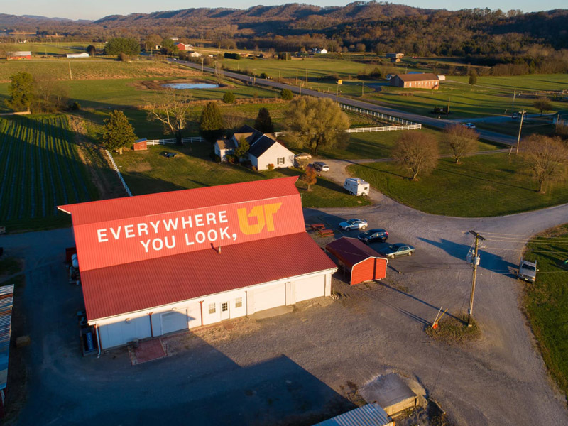 Aerial photo of a green, hilly landscape, with a large red-roofed barn in the foreground.