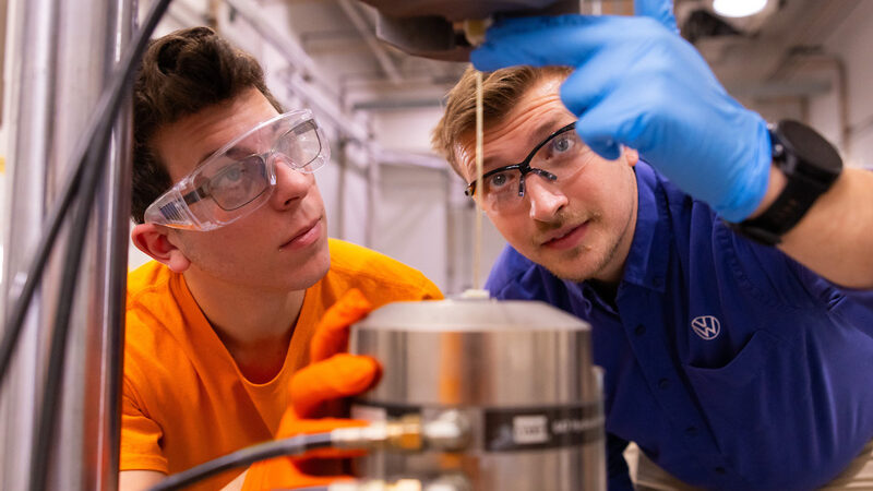 William Henken, a Volkswagen Doctoral Fellow, wearing a VW shirt, with a student about tensile testing of glass fiber reinforced polymeric (GFRP) composites in a lab inside the Science & Engineering Building SERF 104 105 on December 02, 2022. (Photo by Steven Bridges)