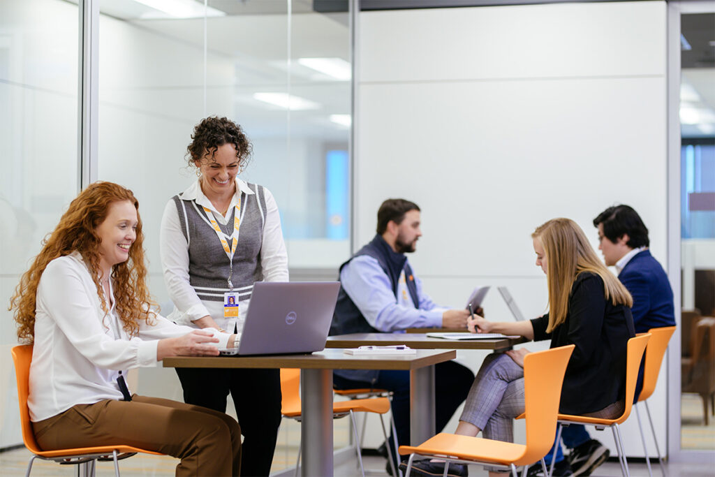 A group of people talking and working on laptops white sitting in a shared break room.