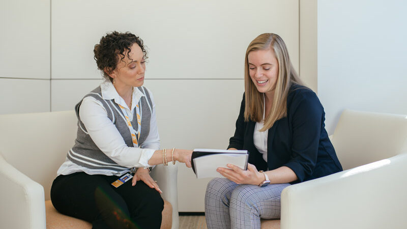 Two UT System employees sitting together while looking at a document.