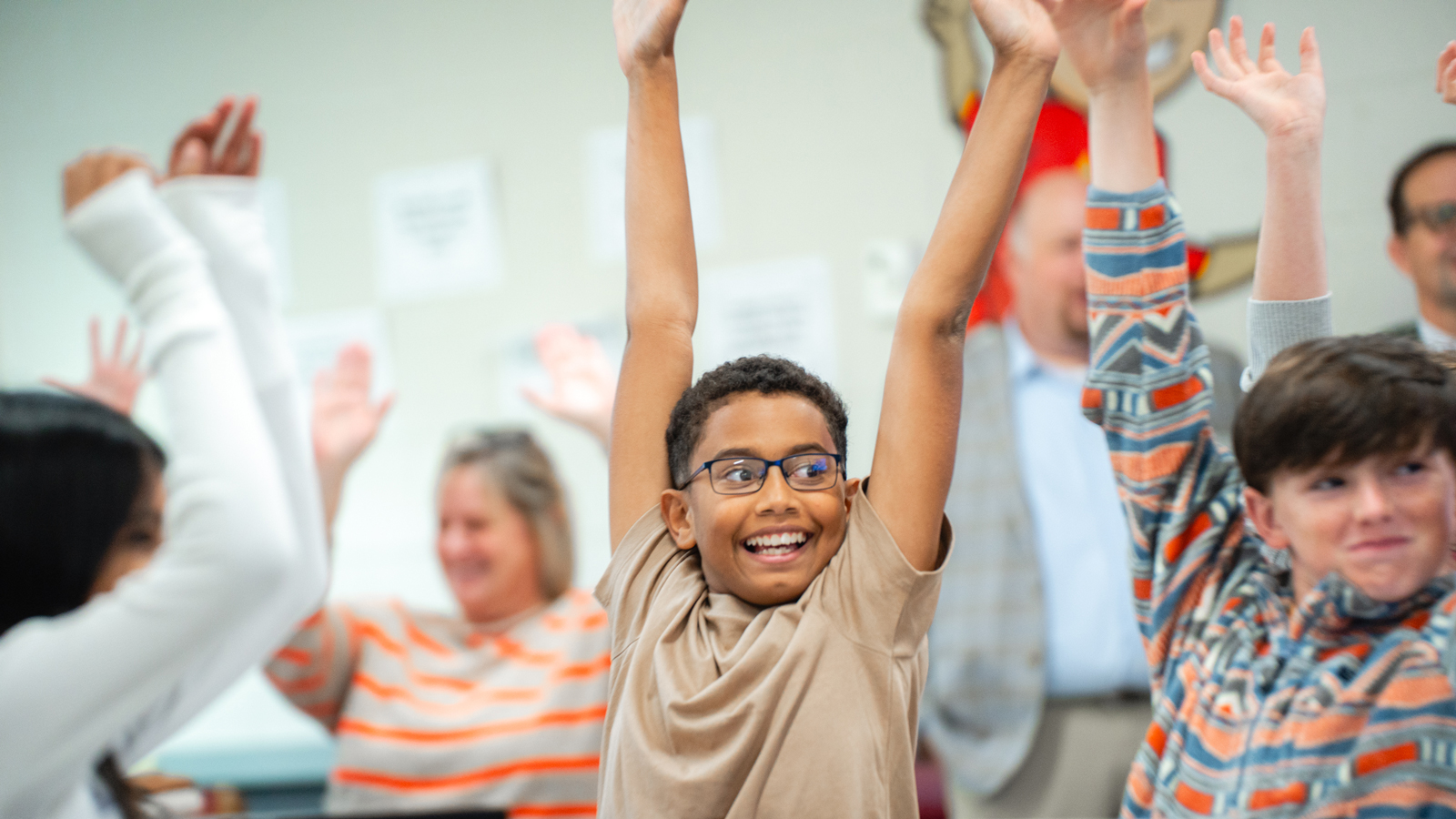 Smiling students raising their hands in class.