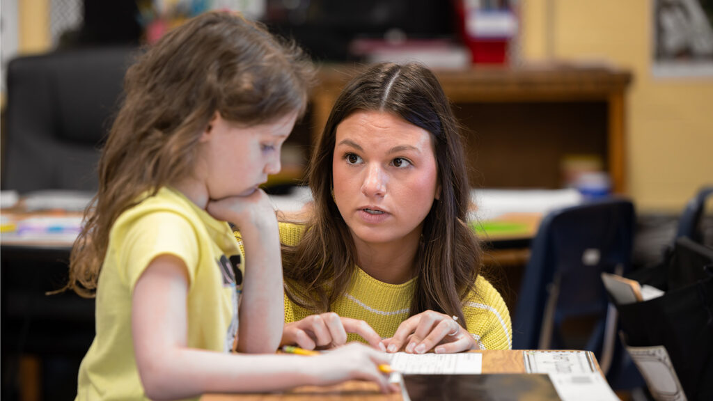 A teacher works one-on-one with an elementary school student in a classroom.