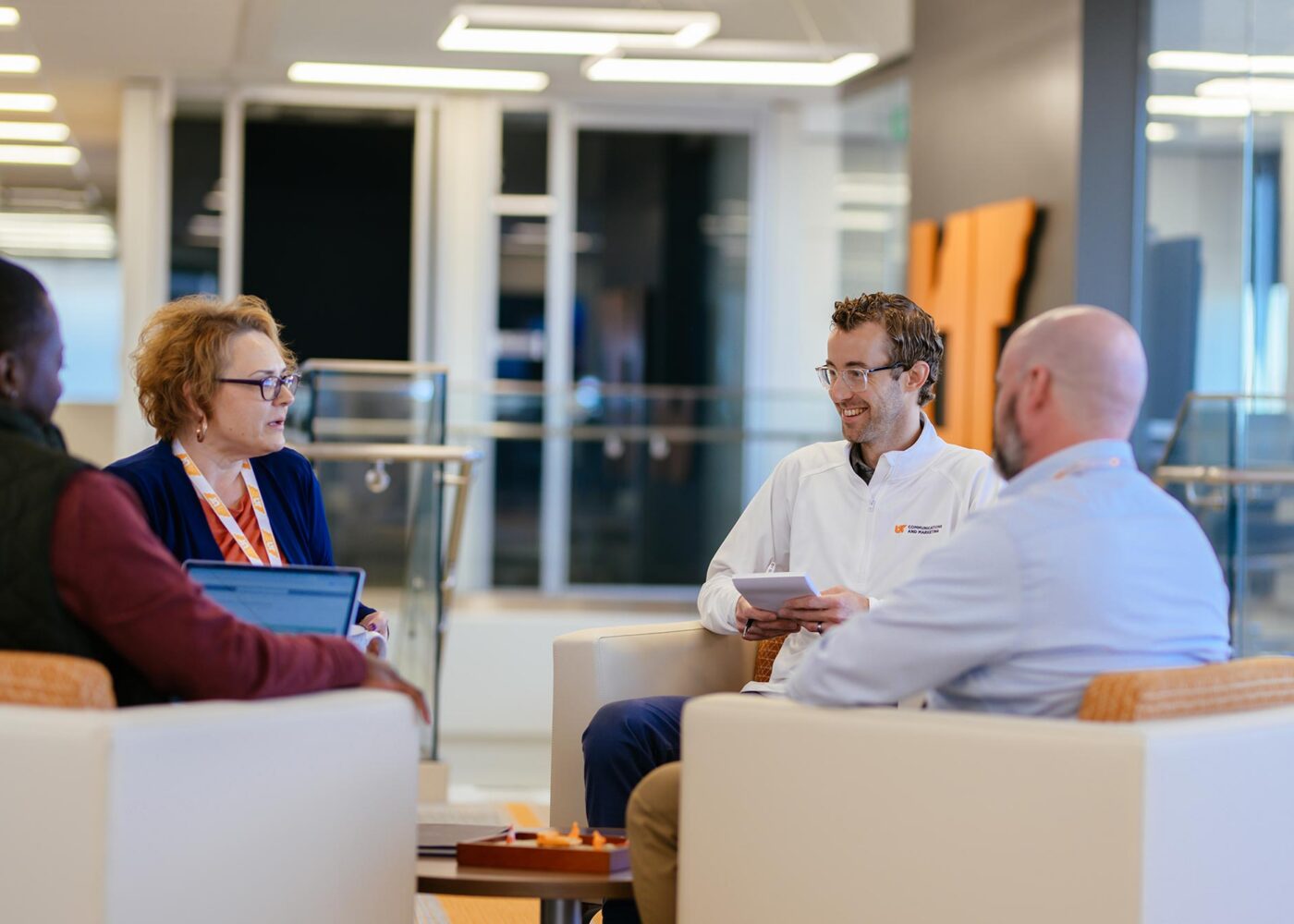 A group of men and women sitting and talking in an office lounge area.