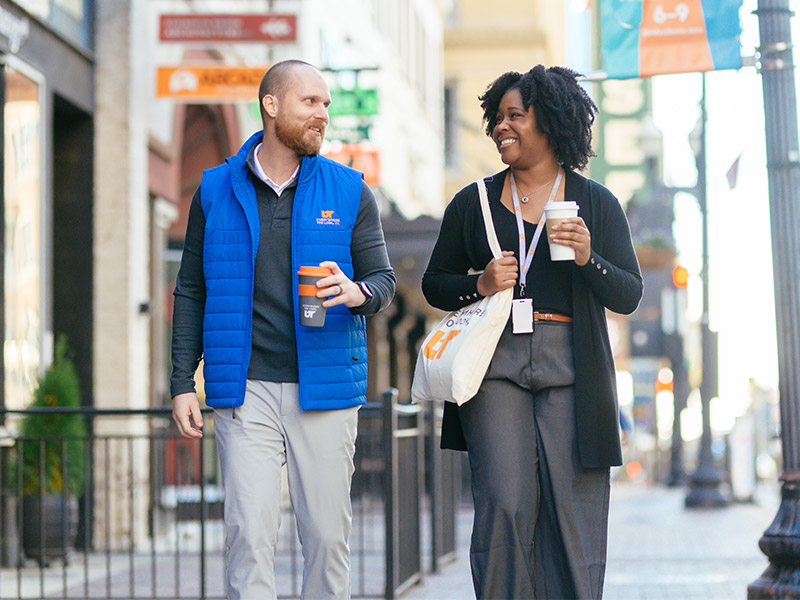 A man and woman walking downtown while having a conversation.